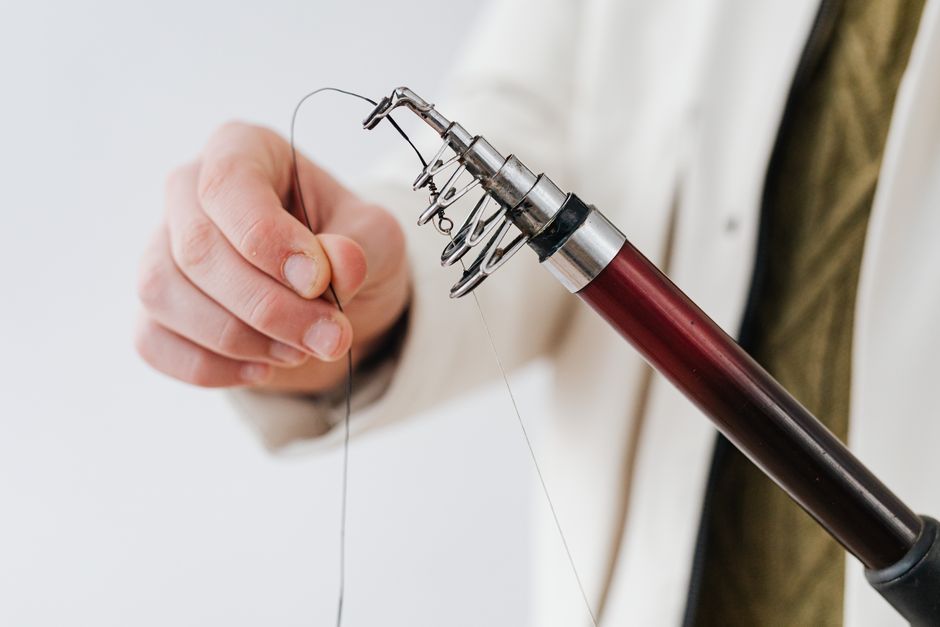 Detailed shot of a hand preparing a fishing rod with line indoors.